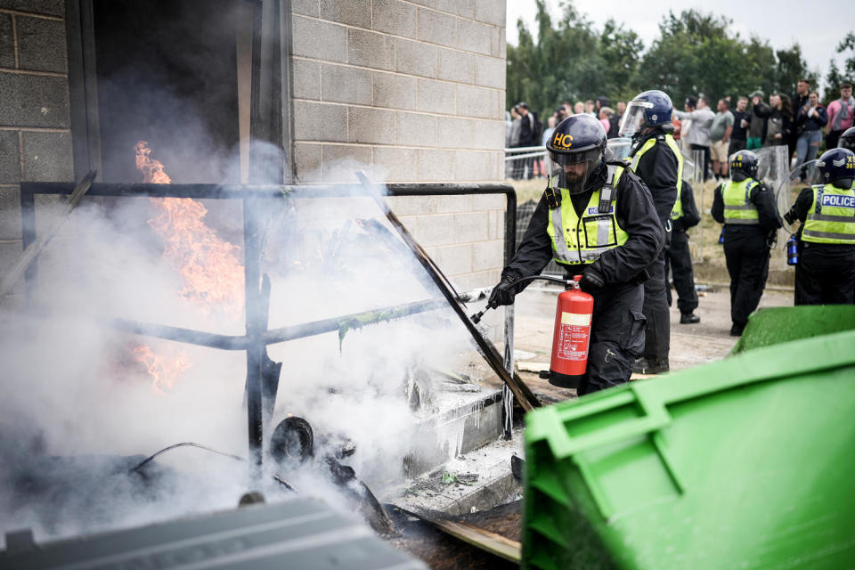 A riot police officer uses a fire extinguisher on a fire in front of a smoking door (Christopher Furlong/Getty Images)