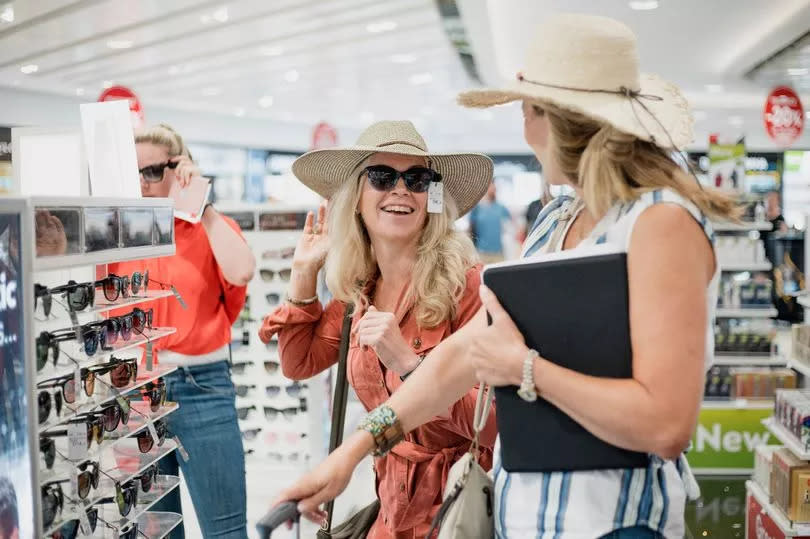 Mature woman are being playful while trying on sunglasses in Duty Free at the airport.