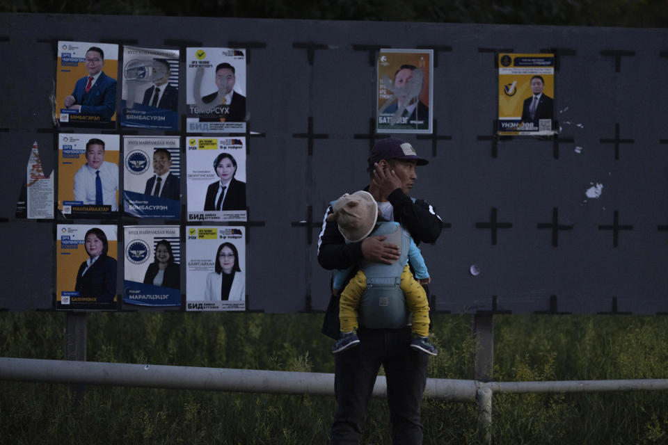 FILE - A man carries a child near candidates' posters two days before polls open in Ulaanbaatar, Mongolia, June 26, 2024. Even in a busy year of elections, the next few days stand out. Voters go to the polls over the next week in fledgling democracies like Mauritania and Mongolia, in the Islamic Republic of Iran and in the stalwart democracies of Britain and France. (AP Photo/Ng Han Guan, File)