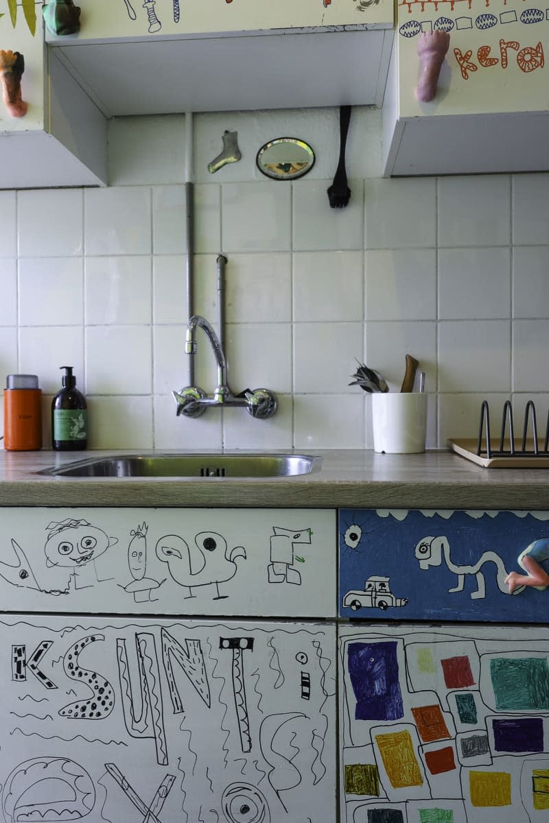 sink area of white tiled kitchen with doodles on cabinets