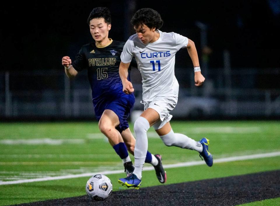 Curtis midfielder Julian Valencia (11) races down the sideline with the ball as Puyallup defender Jet Hazen (15) tries to steal the ball from him during the second half of a 4A Pierce County League boys varsity soccer game at Sparks Stadium in Puyallup, Wash. on May 1, 2023. The teams tied the game 2-2.