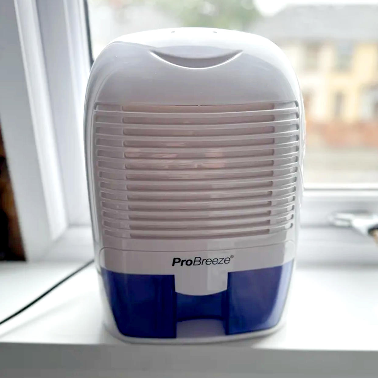  The white and purple ProBreeze 1500ml Mini dehumidifier on a white windowsill. 