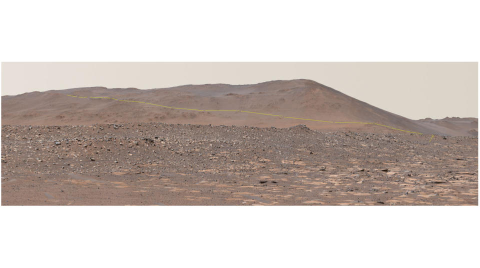 a mars mountain rises in the distance, with red dirt and boulders in the foreground.
