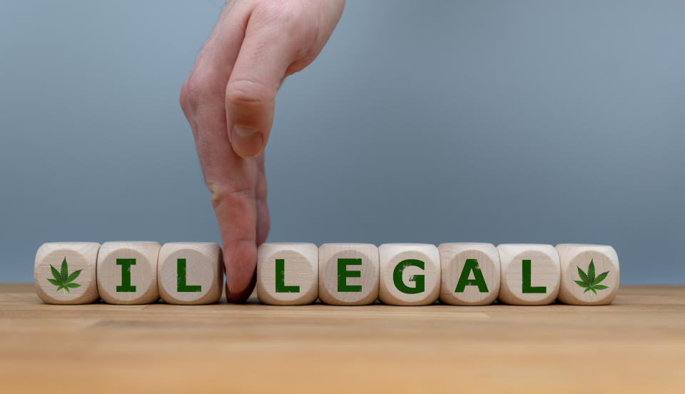 Dice with marijuana leaves and letters spelling "illegal" with a hand between the two dice with the letter "L" on them.