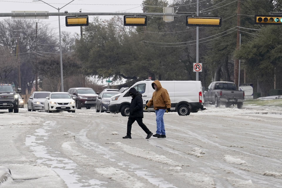 A pair of pedestrians cross a road as drivers make their way down slush and icy road conditions, Wednesday, Feb. 1, 2023, in Dallas. (AP Photo/Tony Gutierrez)