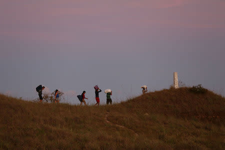 People walk through a field with their belongings, as they try to cross the border between Brazil and Venezuela in Pacaraima, Roraima state, Brazil February 24, 2019. REUTERS/Bruno Kelly