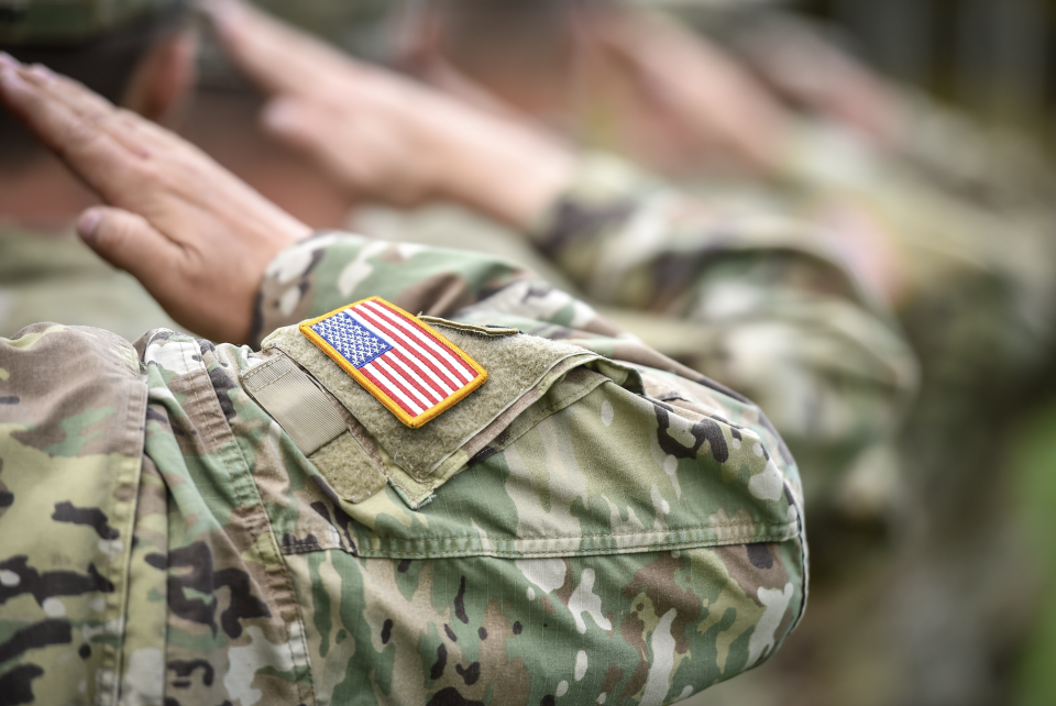 Military personnel in camouflage uniforms saluting, with a close-up of an American flag patch on a sleeve