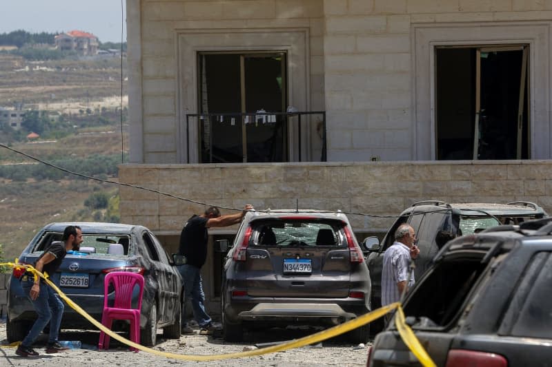 Supporters of Pro-Iranian Hezbollah stand in front of destroyed cars and a building that was heavily hit when Israeli warplanes raided overnight a nearby three-story in the southern Lebanese village of Janata, where at least one person was killed and more than seven others wounded. Marwan Naamani/dpa