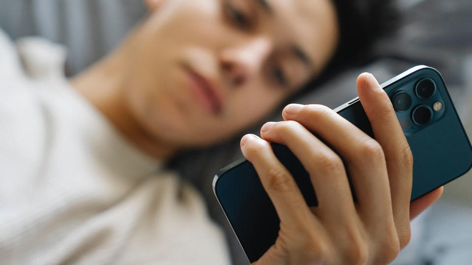 teen holding phone in bed