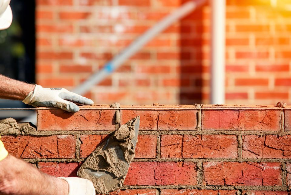 Hard working bricklayer lays bricks on cement mix on construction site. Fight housing crisis by building more affordable houses concept