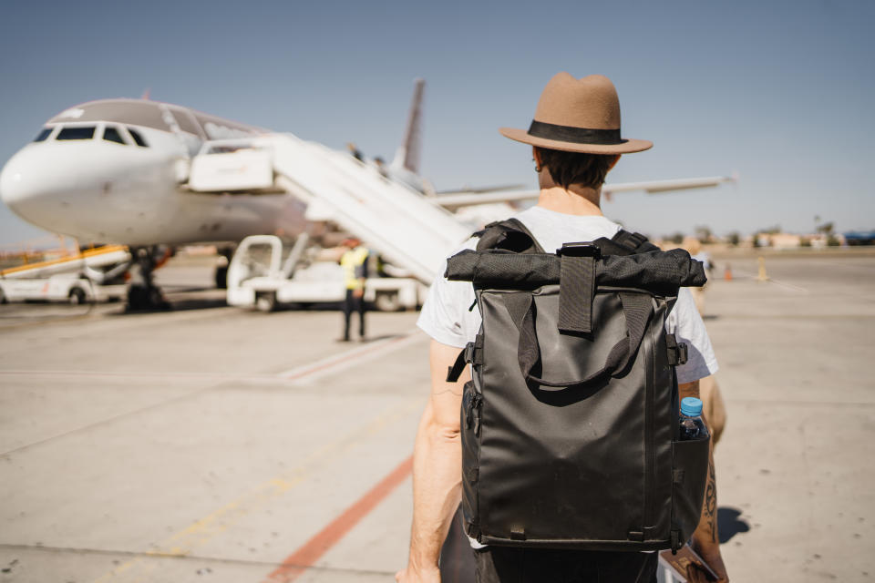 Un joven con sombrero y maleta caminando por el aeropuerto cerca de la pista de despegue. (Getty Creative)