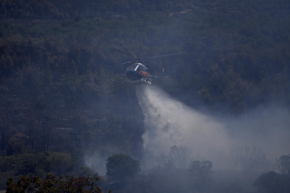 An helicopter drops water on a wildfire near Le Luc, southern France, Thursday, Aug. 19, 2021. A fire that has ravaged forests near the French Riviera for four days is slowing down as winds and hot weather subside, but more than 1,100 firefighters were still struggling to get it under control Thursday, local authorities said. (AP Photo/Daniel Cole)