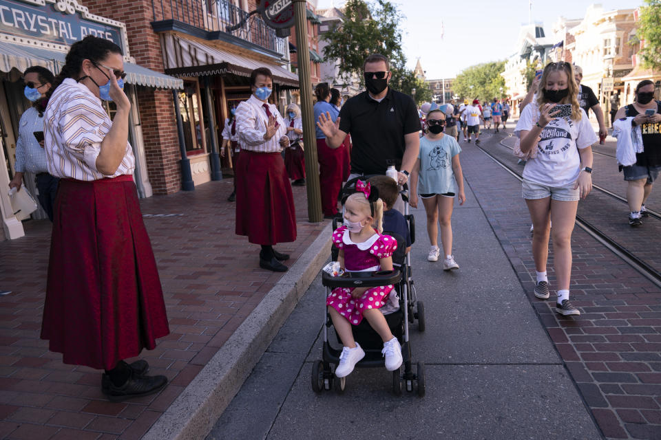 Employees welcome guests at Disneyland in Anaheim, Calif., Friday, April 30, 2021. The iconic theme park in Southern California that was closed under the state's strict virus rules swung open its gates Friday and some visitors came in cheering and screaming with happiness. (AP Photo/Jae C. Hong)