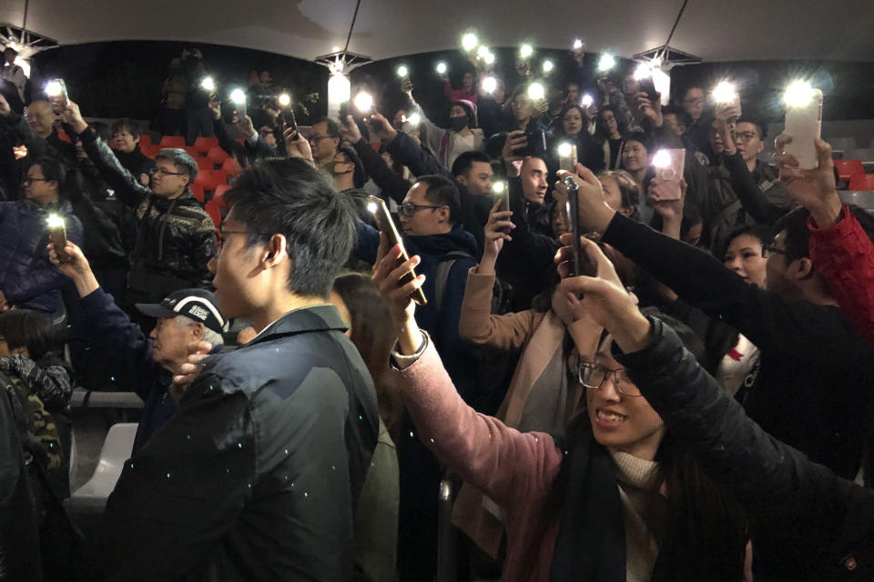 In this Tuesday, Dec. 10, 2019 photo, audience members hold their smartphones aloft after a performance of Les Miserables in at an outdoor event space in Hong Kong. A Hong Kong theater troupe is making audiences weep by touring a stirring production of 'Les Miserables.' Based on Victor Hugo's tale of rebellion in 19th-century France, the rousing music and lyrics of struggle and resistance struck chords with audience members emotionally and physically drained after six months of protests that have convulsed the city. (AP Photo/John Leicester)