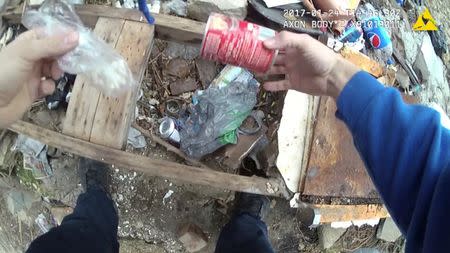 A still image captured from police body camera video appears to show a Baltimore police officer retrieving a small plastic bag in a trash-strewn yard which was placed earlier by the officer according to the Maryland Office of the Public Defender in this image released in Baltimore, Maryland, U.S. on July 19, 2017. Courtesy Baltimore Police Department/Handout via REUTERS