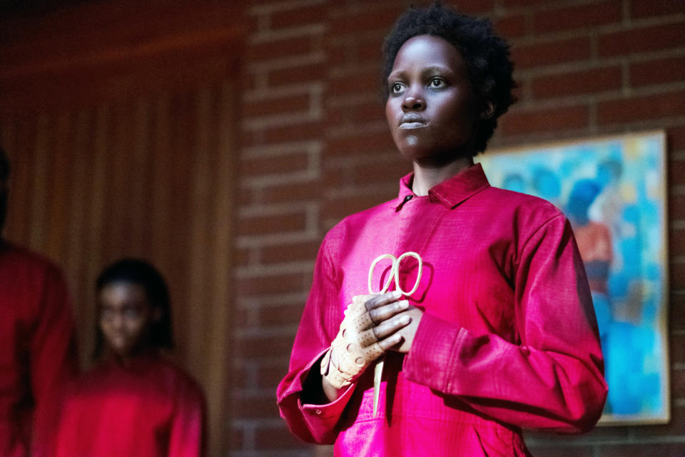 Lupita Nyong'o holds a pair of gold scissors