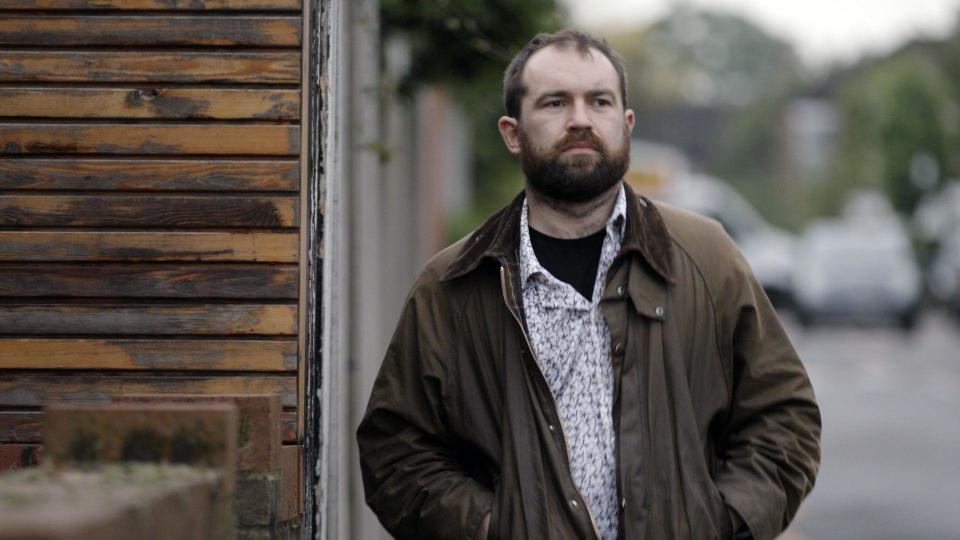 The BBC's undercover reporter, Max, a man with brown hair and a beard, walking down the street with his hands in the pockets of his jacket