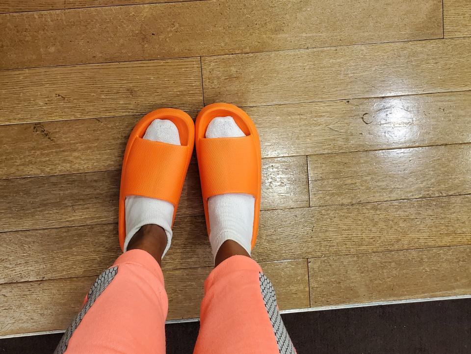 Sandra wearing orange Adidas yeezy slides on hardwood floor