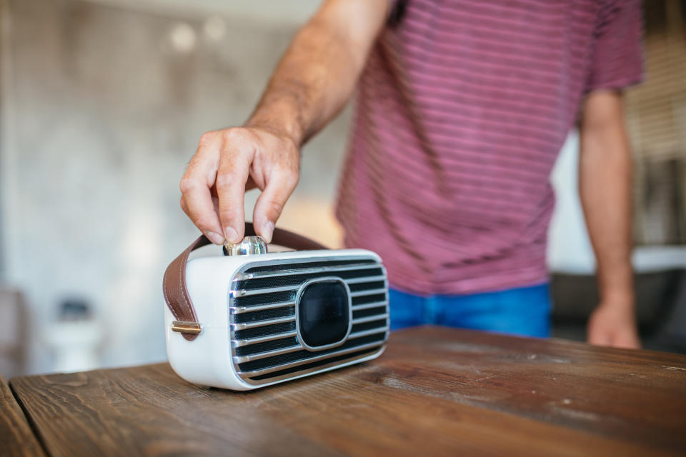 A person wearing a striped shirt adjusts a small, vintage-style radio on a wooden table