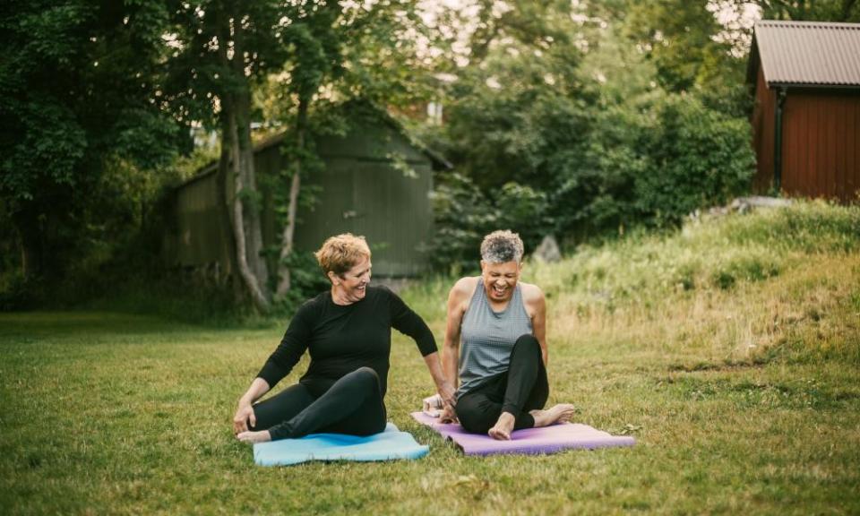 Smiling woman assisting friend while exercising on mat in public park