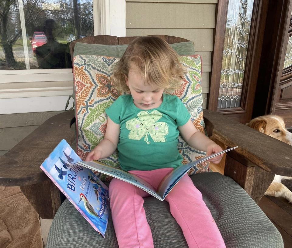 Three-year-old Elsie and her grandmother's dog Bindi spend reading time together. She loves being registered in Dolly Parton's Imagination Library program and receiving free books in the mail.