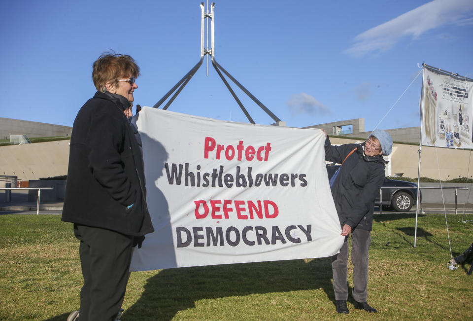 Demonstrators hold a banner during a protest outside Parliament House in Canberra, Australia, Thursday, June 17, 2021 against the prosecution of lawyer Bernard Collaery whose picture is on the demonstrator's shirt. Critics of the secret prosecutions of a former Australian spy and his lawyer argue they are another example of a government concealing political embarrassment under the guise of national security. (AP Photo/Rod McGuirk)