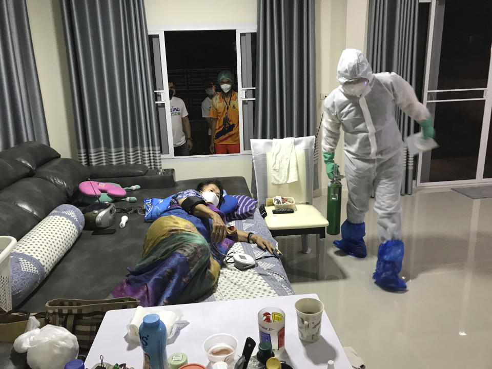 A volunteer from the "Saimai Will Survive" group in protective gear brings in an oxygen tank for an ailing woman infected with COVID-19 Friday, July 23, 2021, in Bangkok, Thailand. As Thailand's medical system struggles beneath a surge of coronavirus cases, ordinary people are helping to plug the gaps, risking their own health to bring care and supplies to often terrified, exhausted patients who've fallen through the cracks. (AP Photo/Tassanee Vejpongsa)