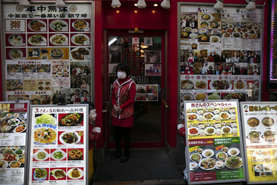 In this Feb. 13, 2020, photo, a restaurant worker wearing a mask stands in front of a Chinese restaurant clustered with photos of the menu items in Yokohama's Chinatown, near Tokyo. A top Olympic official made clear Friday the 2020 Games in Tokyo will not be cancelled despite the virus that has spread from China. (AP Photo/Jae C. Hong)