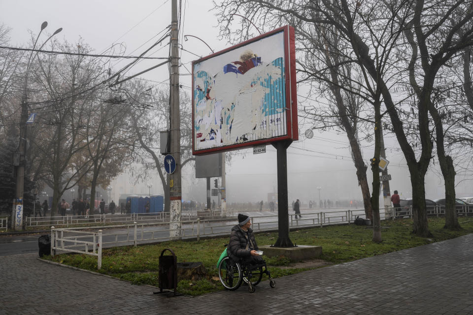 FILE - A man begs for alms under a billboard with visible remains of Russian posters in downtown Kherson, southern Ukraine, Nov. 21, 2022. (AP Photo/Bernat Armangue, File)