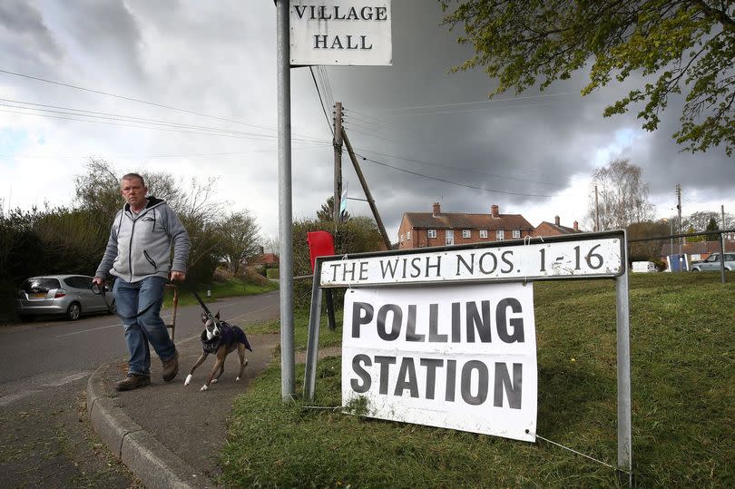 A man walks his dog past a polling station sign in Kenardington near Ashford