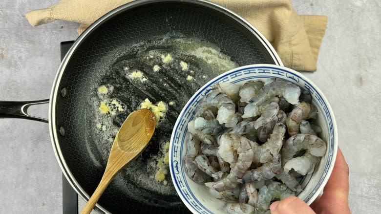 hand putting shrimp in pan
