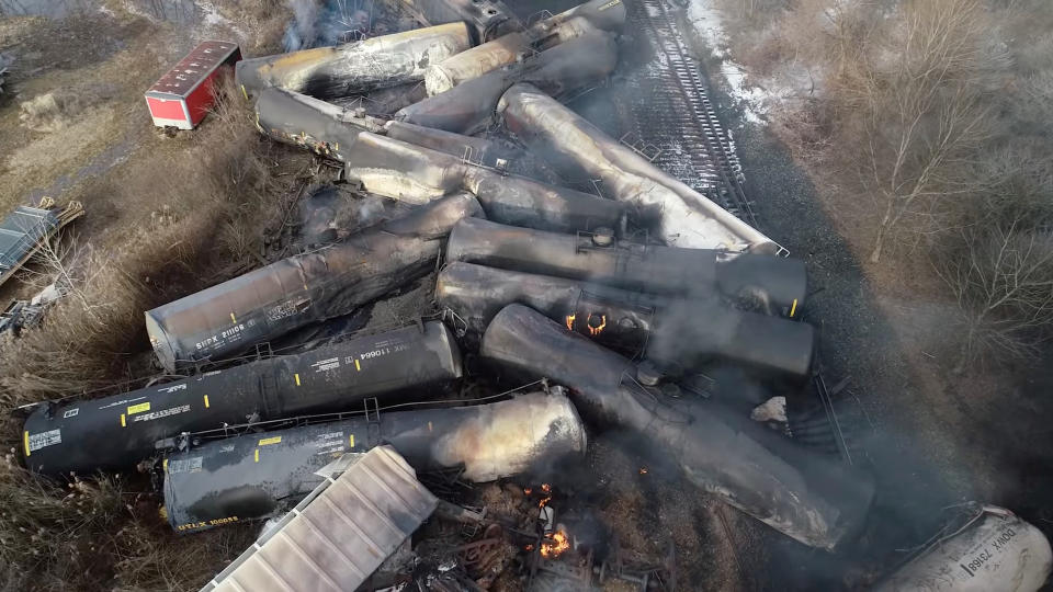 Drone footage shows more than a dozen charred cars of the freight train packed together off the tracks after the derailment.