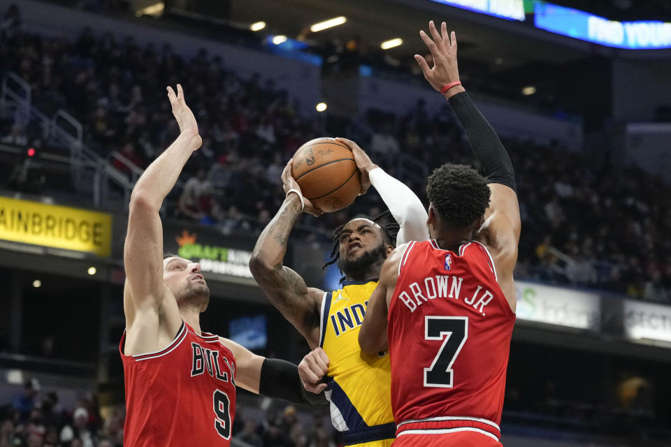 Indiana Pacers forward Oshae Brissett, center, shoots between Chicago Bulls defenders Nikola Vucevic, left, and Troy Brown Jr. during the first half of an NBA basketball game in Indianapolis, Friday, Feb. 4, 2022. (AP Photo/AJ Mast)