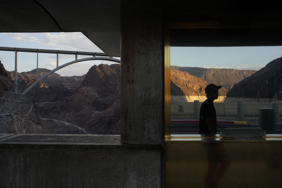 A person is reflected in a window as they walk across Hoover Dam at Lake Mead, Sunday, June 26, 2022, near Boulder City, Nev. The bathtub ring of light minerals around Lake Mead shows the high water mark of the reservoir which has fallen to record lows. (AP Photo/John Locher)