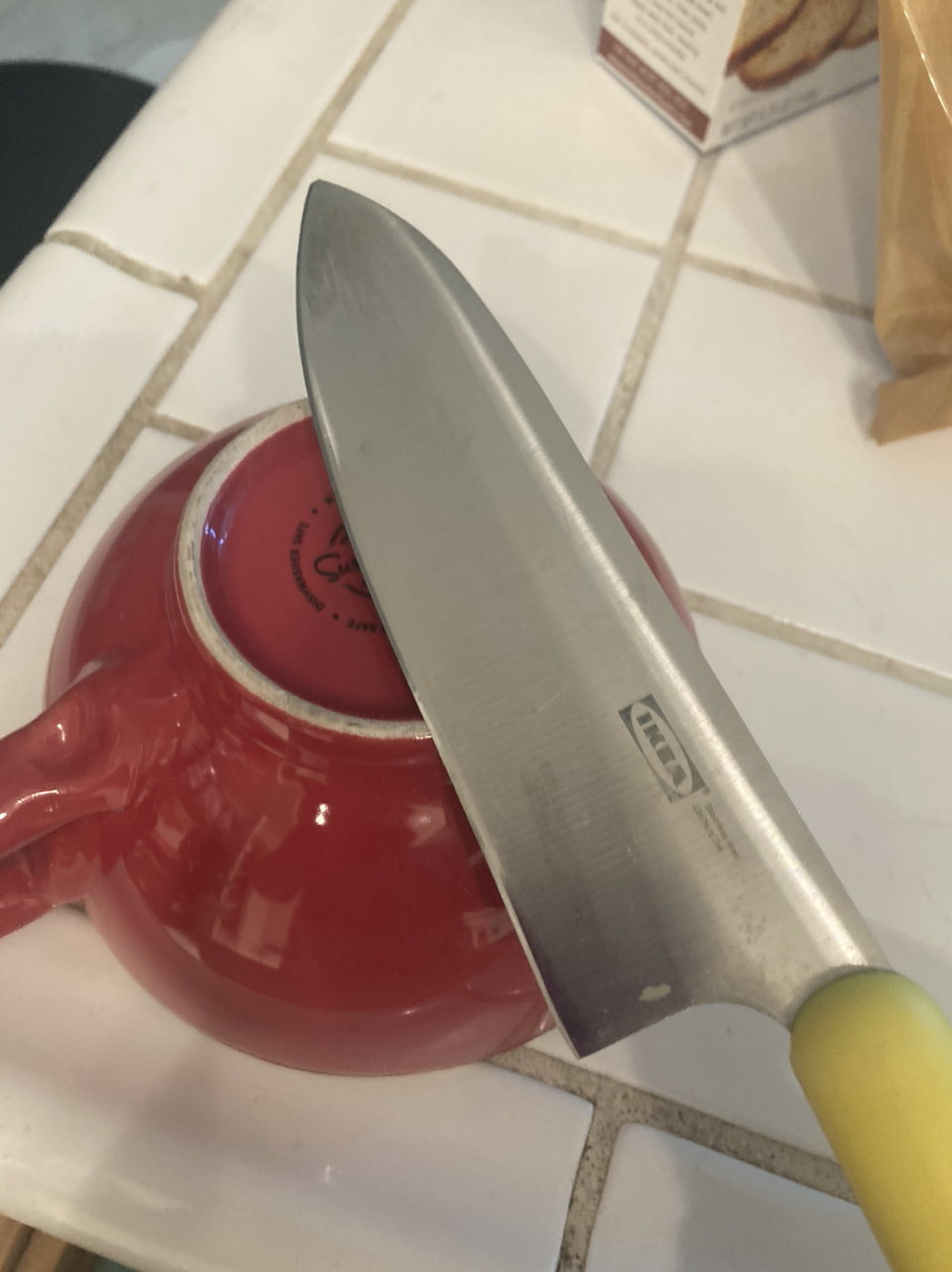 Knife resting on red teapot on a tiled counter