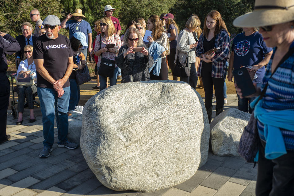 People take pictures of a plaque on a boulder with the names of victims during the dedication of the Borderline Healing Garden at Conejo Creek Park in Thousand Oaks, Calif., Thursday, Nov. 7, 2019. The dedication marked the anniversary of a fatal mass shooting at a country-western bar a year earlier. (Hans Gutknecht/The Orange County Register via AP)