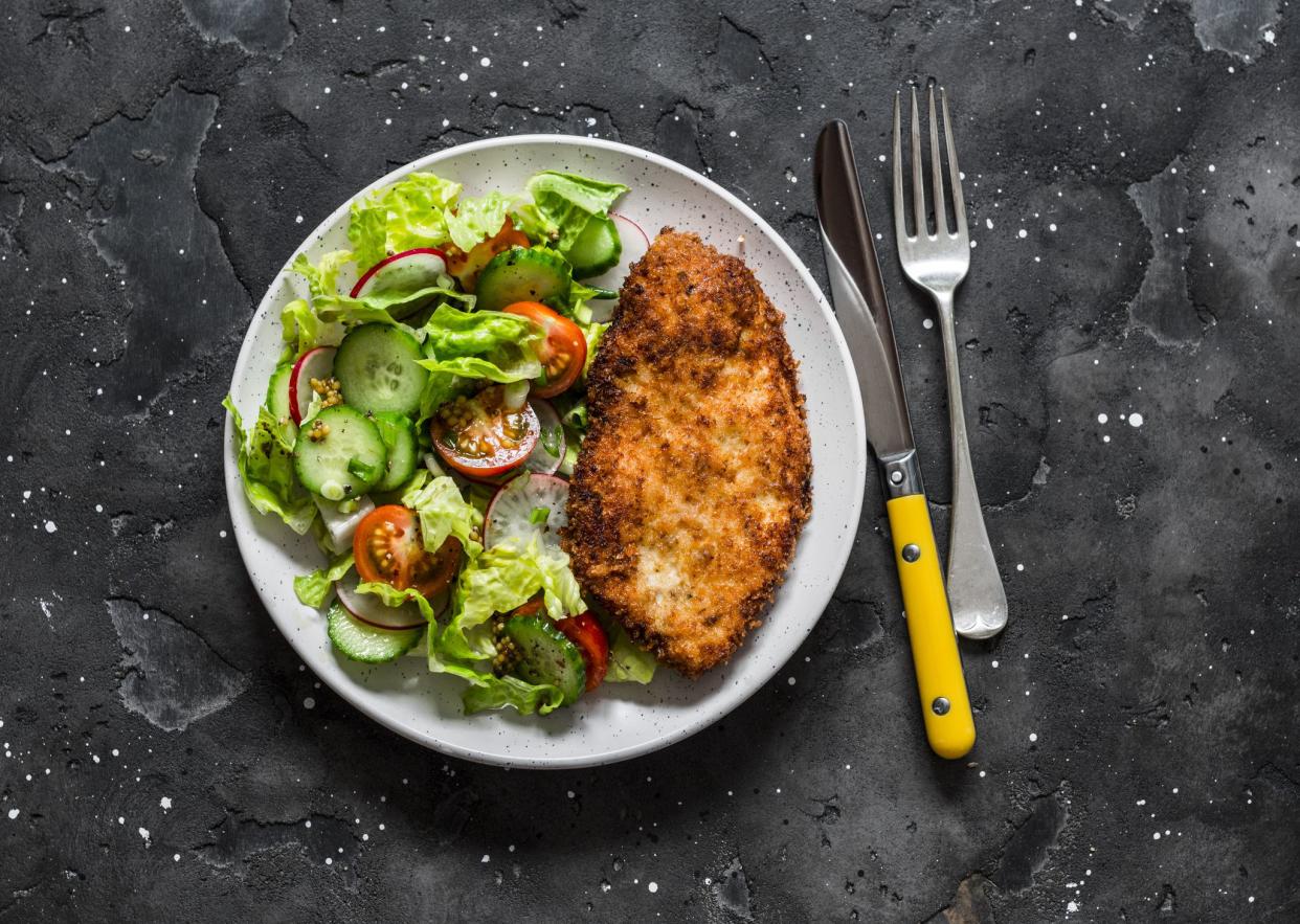 Chicken milanese and fresh romaine salad, cherry tomatoes, radishes, cucumbers salad - delicious lunch on a dark background, top view