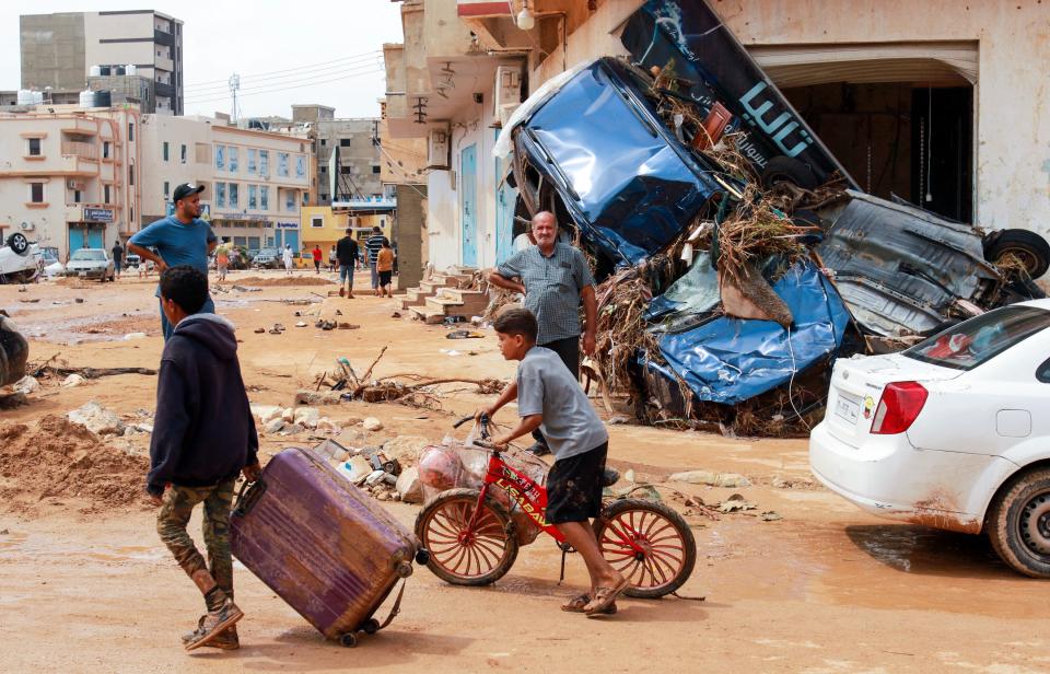 A boy pulls a suitcase past debris, including an upended car, in a flash-flood-damaged area in Derna.
