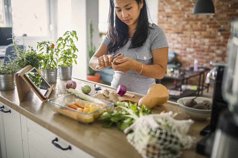 A woman peeling vegetables in her sunny kitchen.