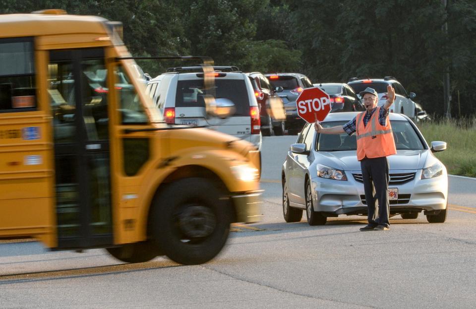 Crossing guard William Gulley waves a bus though near cars bringing children on to Midway Elementary School in Anderson in August. 