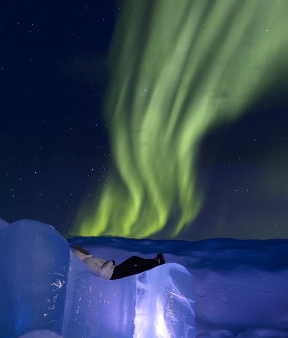 Persona acostada sobre el hielo mirando una aurora boreal
