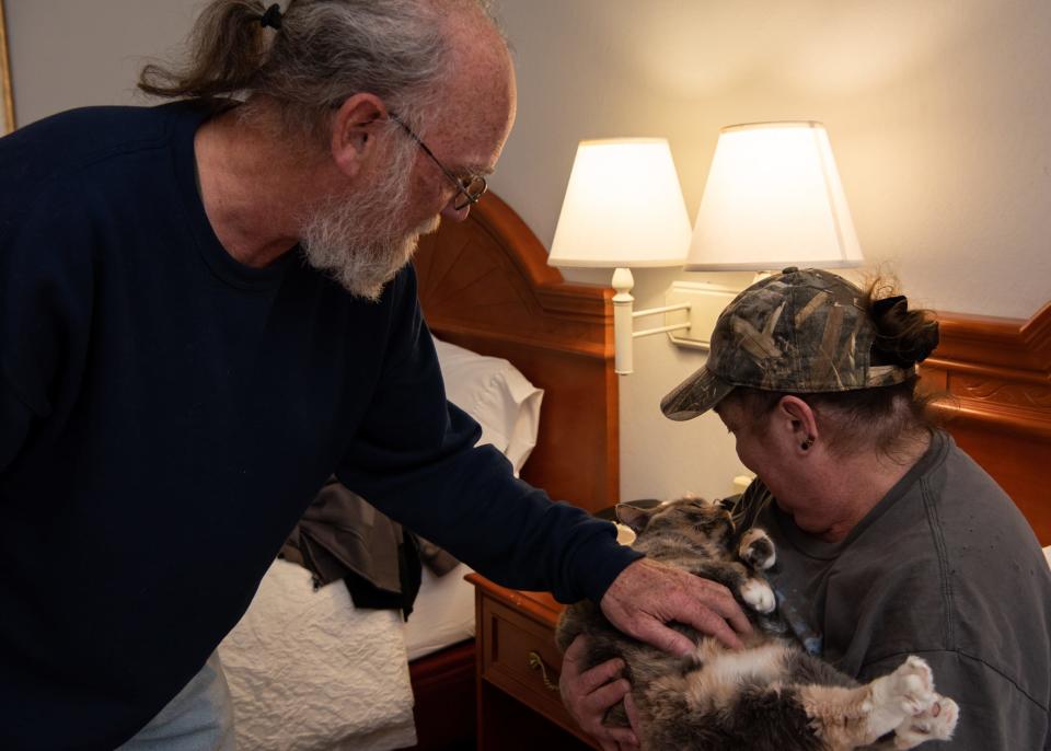 Ron Salamanca, left, and his girlfriend, Christine Hendricks, a displaced couple from the Bush House Hotel, show their cat, Gypsie, some affection while sitting in their hotel room at a Hampton Inn in Quakertown on Tuesday, December 7, 2021.