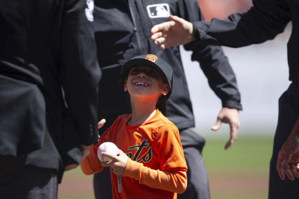 Seven-year-old Little Leaguer James Mims, of Richmond, Calif., is dwarfed by the umpires as he and his teammates took the field before a baseball game between the San Diego Padres and San Francisco Giants, Sunday, April 7, 2024, in San Francisco. (AP Photo/D. Ross Cameron)