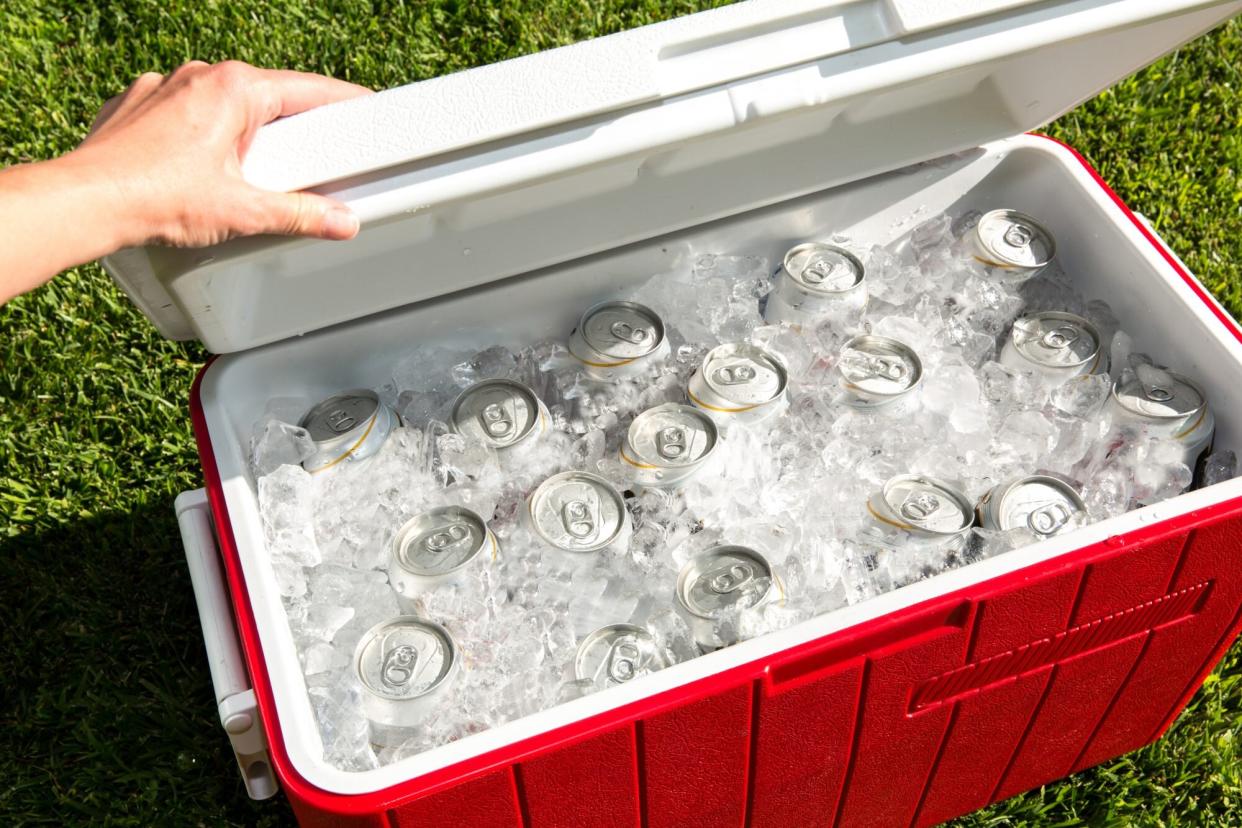 red cooler outside on grass filled with ice and cans
