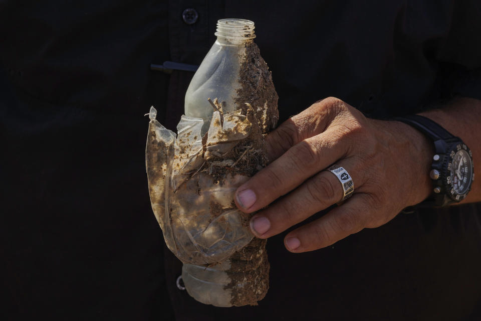 Jim Hogg County Sheriff's Investigator Ruben Garza holds empty water bottles as he investigates the location of a missing water station for immigrants containing sealed jugs of fresh water along a fence line near a roadway in rural Jim Hogg County, Texas, Tuesday, July 25, 2023. The South Texas Human Rights Center maintains over 100 blue barrels consistently stocked with water across rural South Texas to serve as a life-saving measure for immigrants who have crossed into the United States to travel north in the sweltering heat. (AP Photo/Michael Gonzalez)