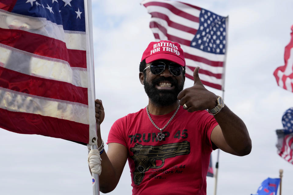 Enzo Alcindor, a supporter of former President Donald Trump, gestures to passersby as he sits on his vehicle with flags outside of Trump's Mar-a-Lago estate, Monday, March 20, 2023, in Palm Beach, Fla. (AP Photo/Lynne Sladky)