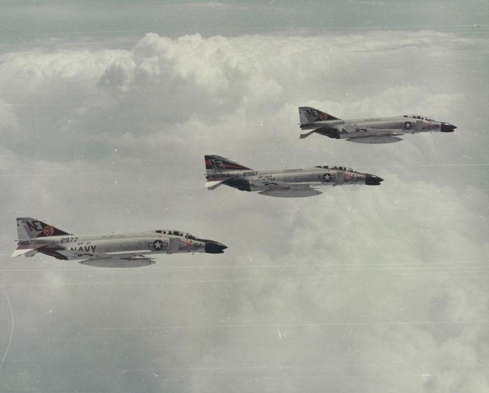 3 US Navy, McDonnell Douglas F-4 Phantom II airplanes, in flight, with clouds in the distance, photographed during the Vietnam War, 1965.