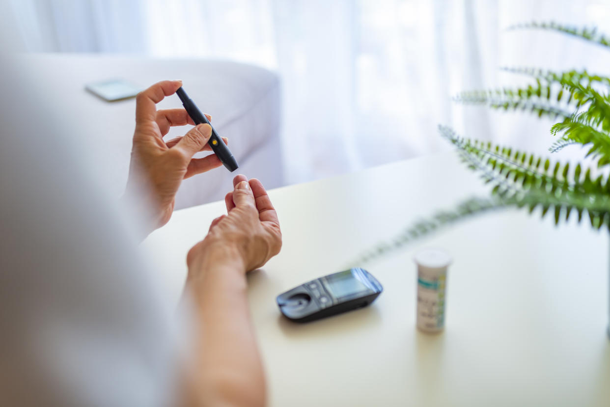 Close up of mature woman hands using lancet on finger to check blood sugar level by Glucose meter, Healthcare Medical and Check up, Medicine, diabetes, glycemia, health care and people concept