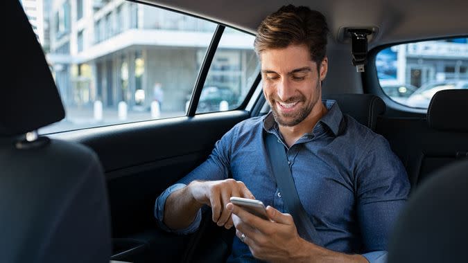 Happy smiling businessman man typing message on phone while sitting in a taxi.