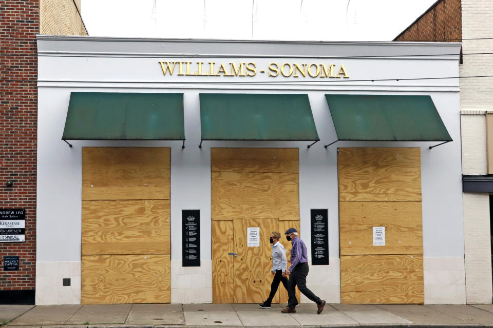 A couple walks in the Shadyside shopping district of Pittsburgh past a Williams-Sonoma store that is boarded up temporarily due to social distancing mandated due to COVID-19 on Wednesday, April 29, 2020. (AP Photo/Gene J. Puskar)